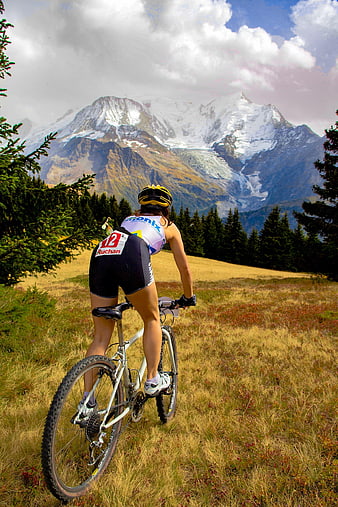 Female mountain biker riding through alpine meadow with snow-capped peaks