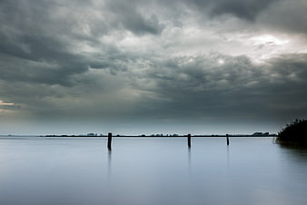 Serene Lake Landscape with Dramatic Clouds and Wooden Posts