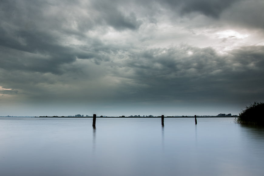 Serene Lake Landscape with Dramatic Clouds and Wooden Posts