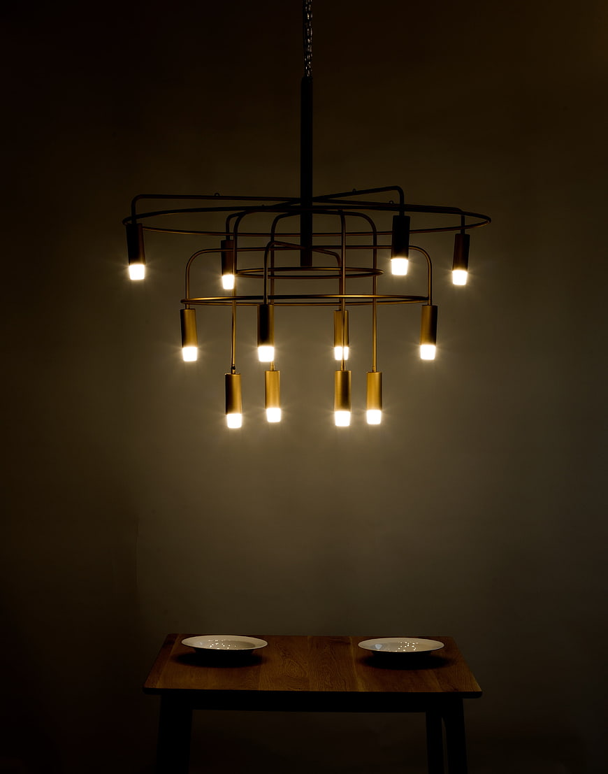 Modern Brass Chandelier With Warm LED Bulbs Over Wooden Dining Table