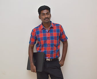 Indian man holding laptop against white wall