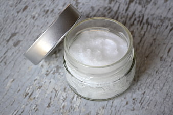 Open glass jar of white coconut oil on rustic wood