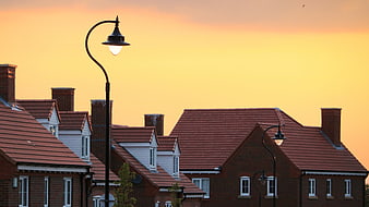 Suburban rooftops and street lamps against a golden sunset sky