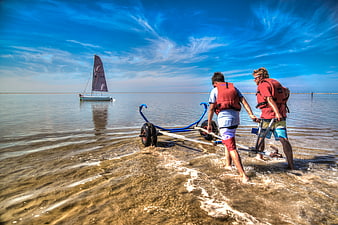 Two Men Launching Sailboat on Shallow Beach