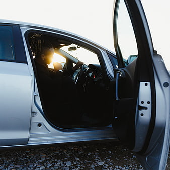 Man sitting in silver car with open door at sunset