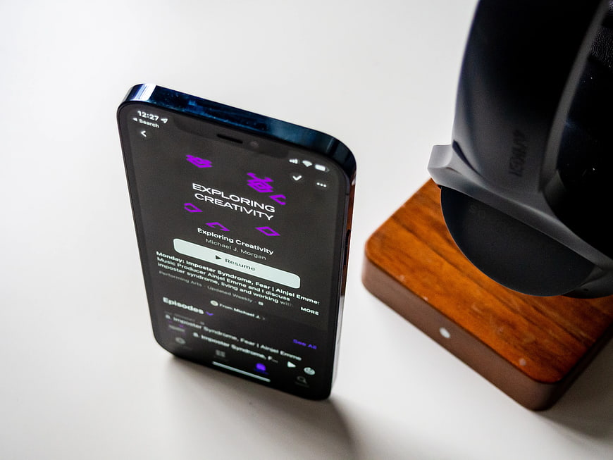 Smartphone Playing Podcast Next to Headphones on Desk