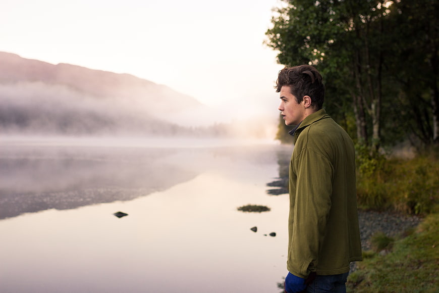 Young man standing by misty lake at sunrise
