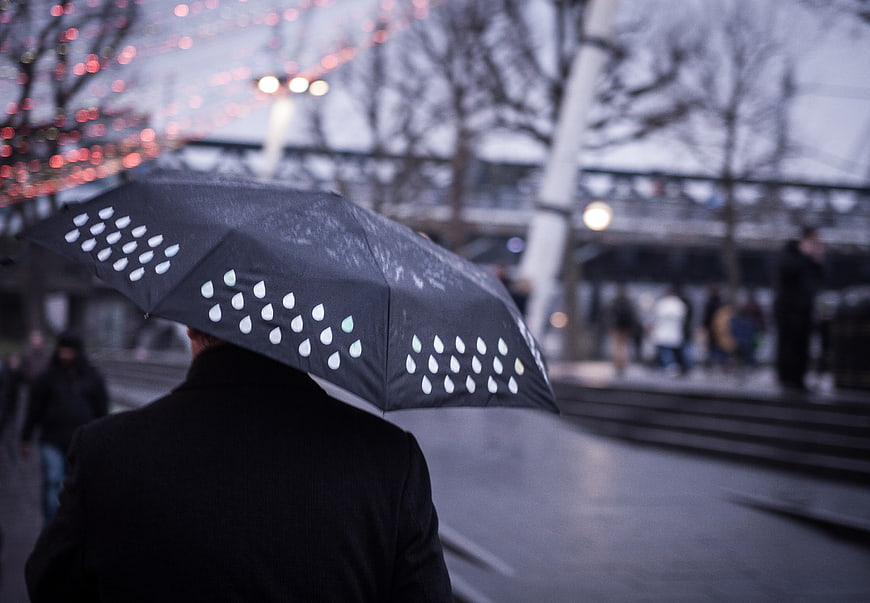 Person with black raindrop pattern umbrella walking in city