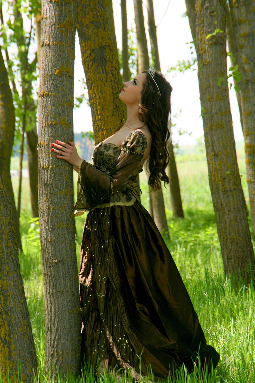 Woman in vintage gown standing in a sunlit forest
