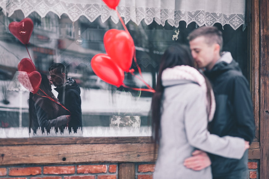 Couple kissing in front of shop window with heart balloons