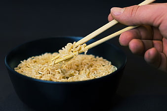 Hand Using Chopsticks to Lift Noodles from Black Bowl