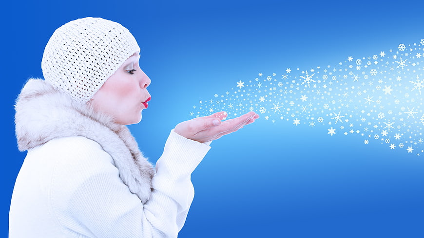 Woman blowing snowflakes from hand on blue background