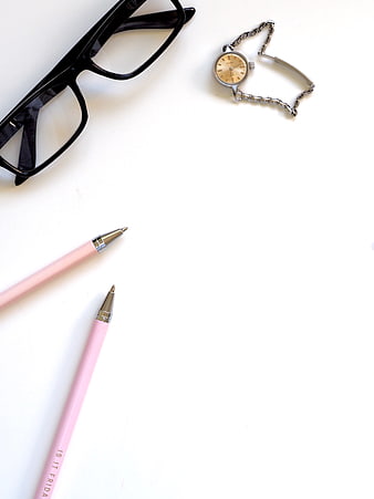 Minimalist flat lay of pink pens, glasses, and watch on white
