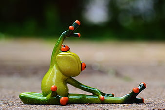 Green ceramic frog figurine doing yoga pose on pavement