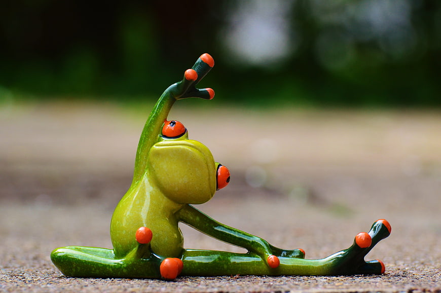 Green ceramic frog figurine doing yoga pose on pavement