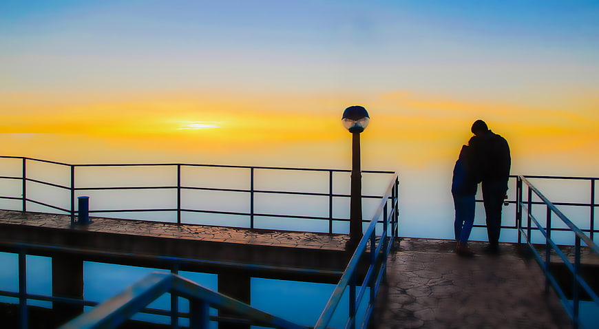 Silhouette of couple embracing on pier at sunset