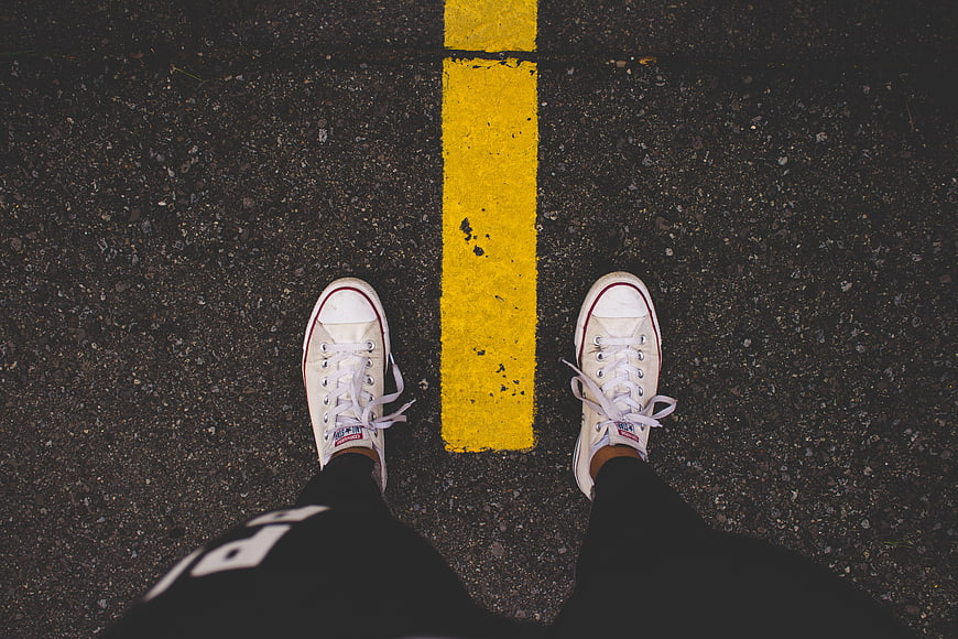 Top View of White Sneakers on Asphalt Road with Yellow Line