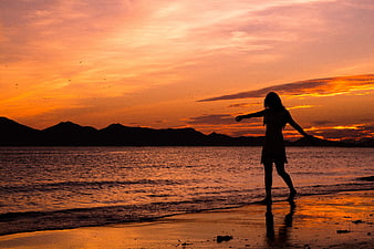 Silhouette of woman walking on beach at sunset