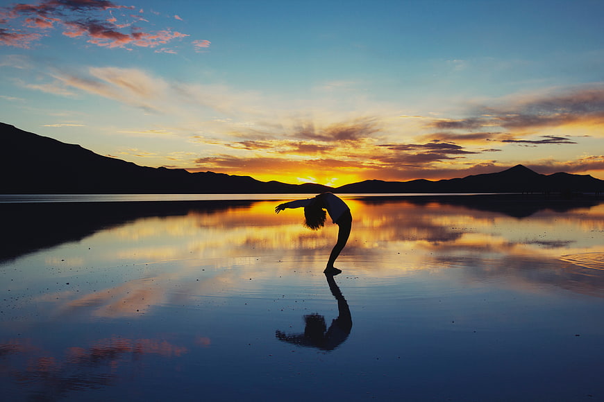 Silhouette of woman stretching on reflective lake at sunset