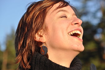Close-up portrait of laughing woman with yin yang earrings outdoors