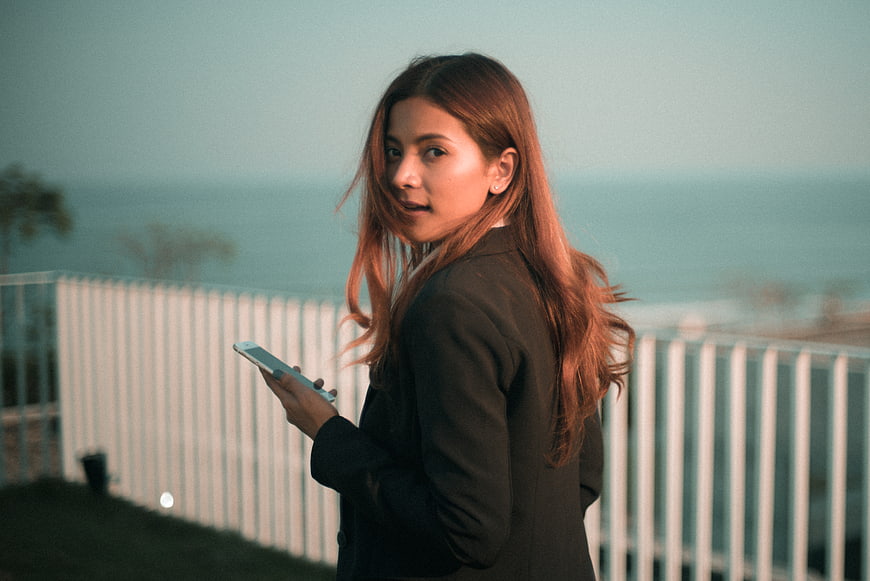 Woman in blazer looking back with smartphone on balcony