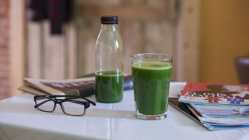 Green vegetable smoothie in glass and bottle on table with reading glasses