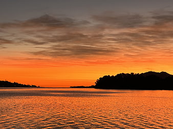 Vibrant Orange Sunset Over Calm Water with Silhouetted Hills
