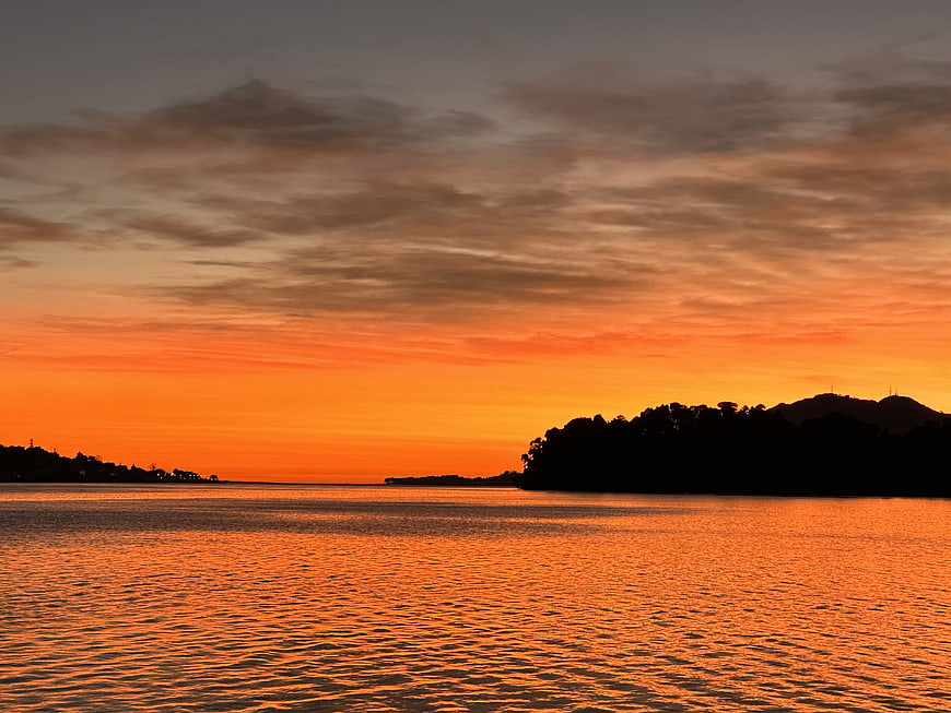 Vibrant Orange Sunset Over Calm Water with Silhouetted Hills