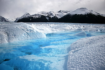 Glacial meltwater stream flowing through ice with snow-capped mountains