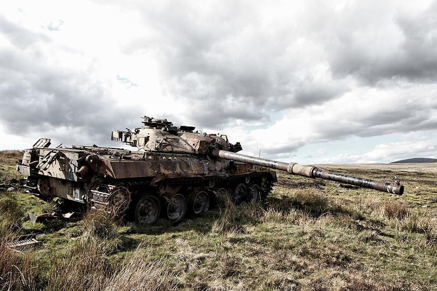 Abandoned rusty tank on grassy moor under cloudy sky