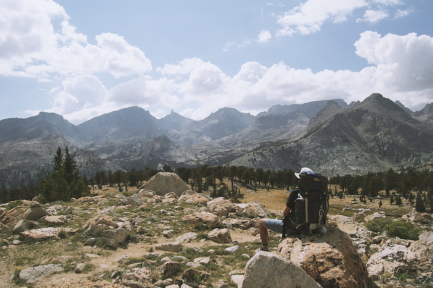 Hiker with backpack sitting on rock overlooking mountain range