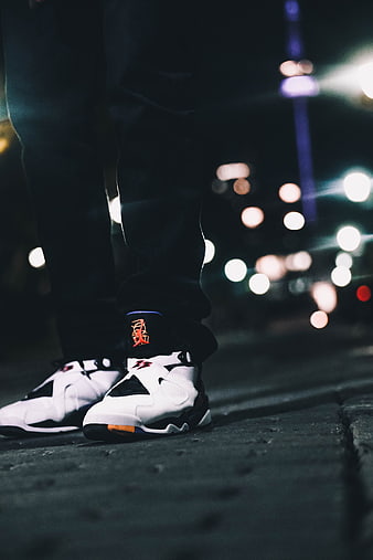 Close-up of white sneakers on city street at night with bokeh