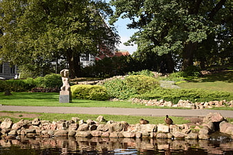 Sculpture in a lush city park with pond and ducks