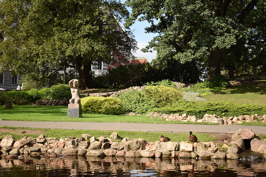 Sculpture in a lush city park with pond and ducks