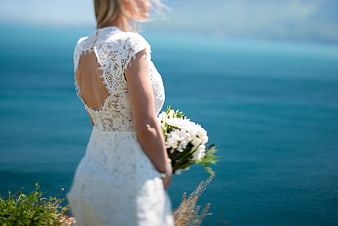 Bride in Lace Dress Holding Bouquet by the Ocean