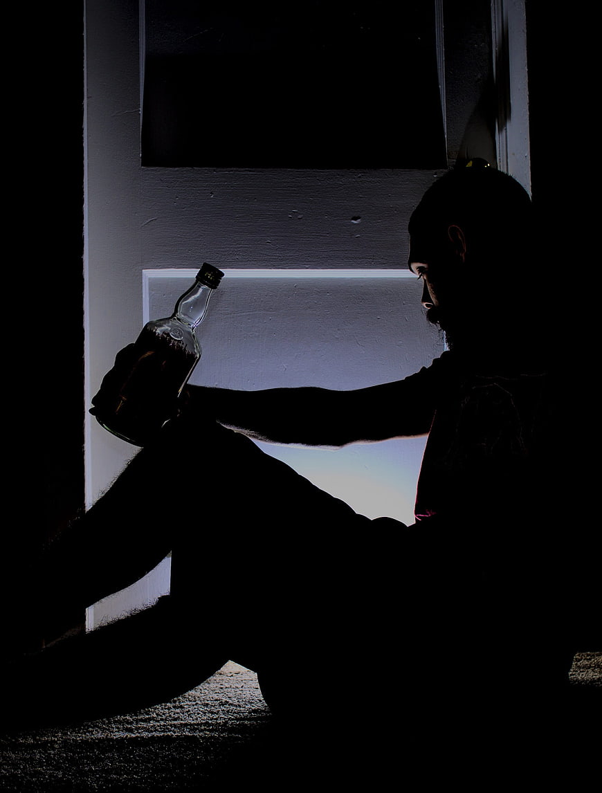 Silhouette of Man Sitting Alone with Alcohol Bottle