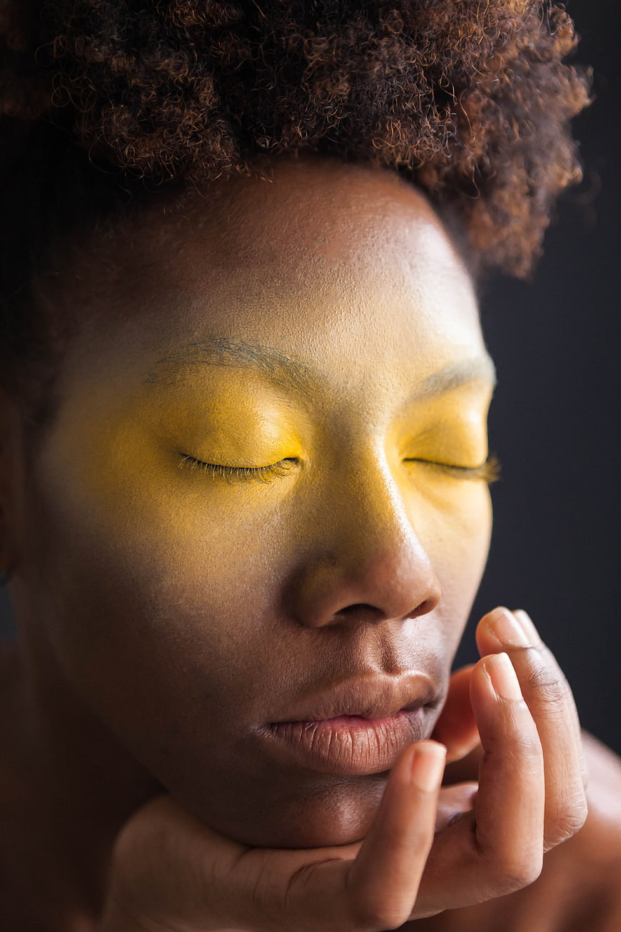 Close-up portrait of woman with yellow light on closed eyes
