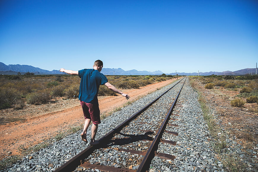 Man balancing on railway tracks in arid landscape