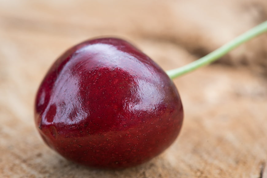 Close-up of a single fresh red cherry on wood