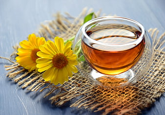 Glass cup of herbal tea with yellow calendula flowers on rustic burlap