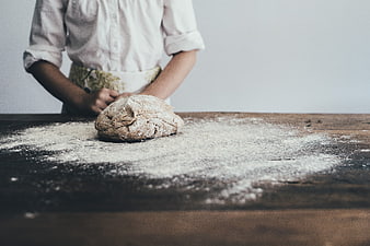 Baker kneading dough on wooden table with flour