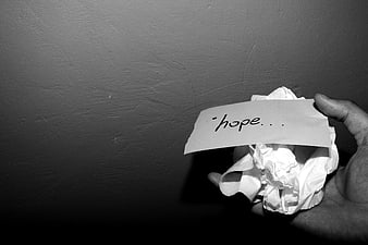 Hand holding crumpled paper with handwritten hope text on dark background