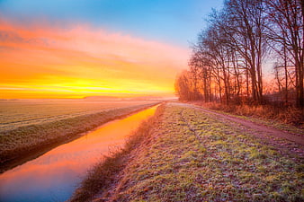 Frosty rural canal path at vibrant sunrise with bare trees