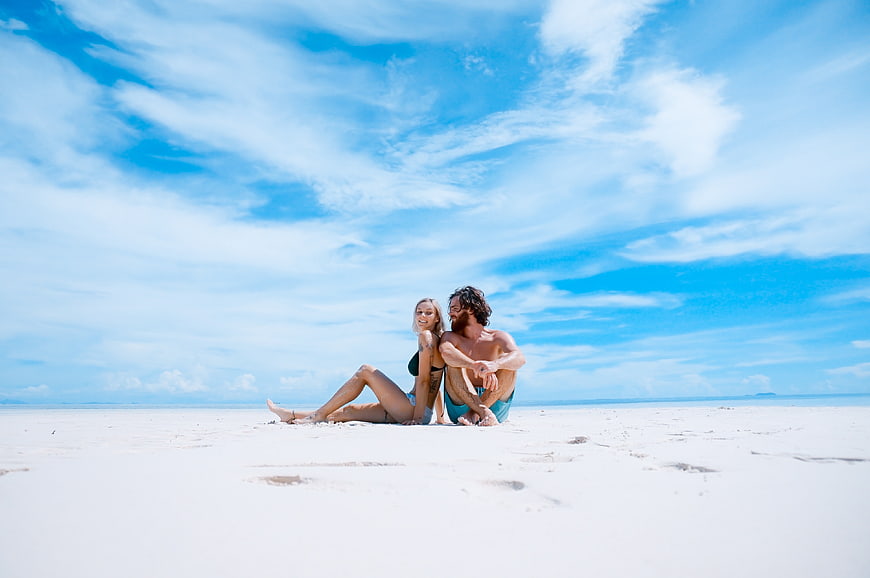 Happy couple relaxing on white sand beach under blue sky