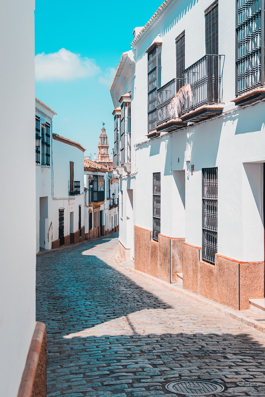 Sunny cobblestone street in white Spanish village with church tower