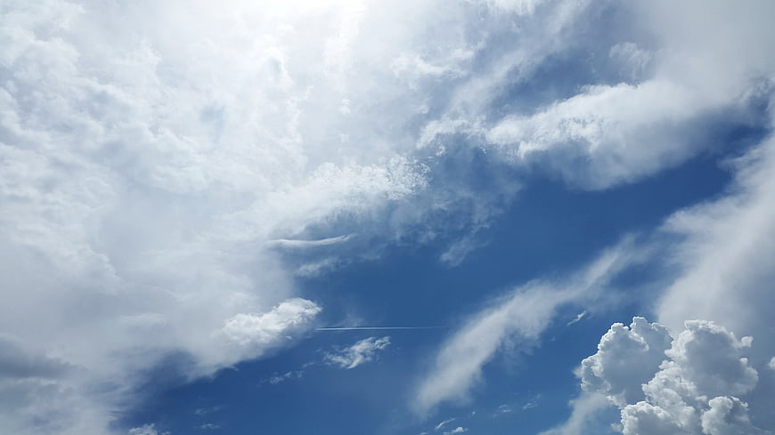 Dramatic blue sky with white clouds and airplane contrail