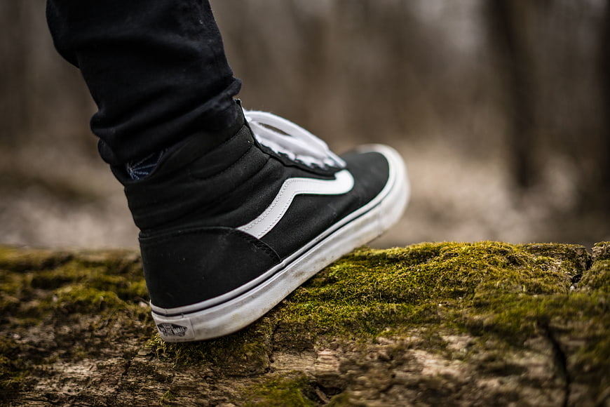 Close-up of black sneaker on mossy log in forest