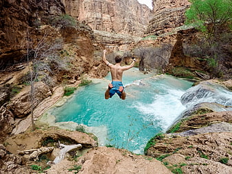 Man jumping into turquoise canyon pool