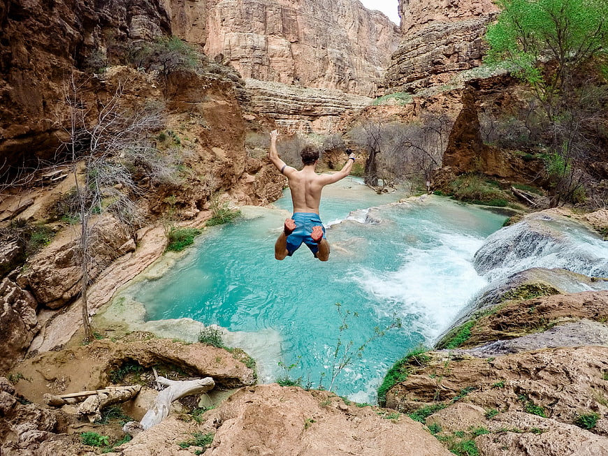 Man jumping into turquoise canyon pool