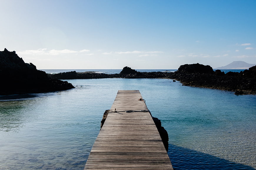 Wooden pier extending into calm turquoise water surrounded by dark volcanic rocks